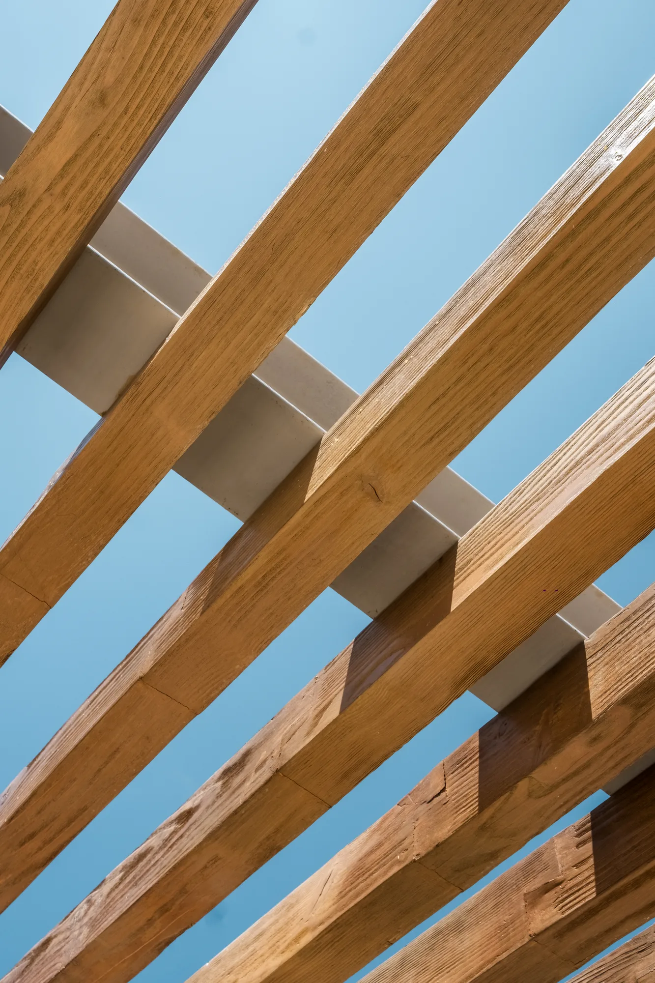 Upward view of a timber pergola, its wood beams crossing against a blue sky