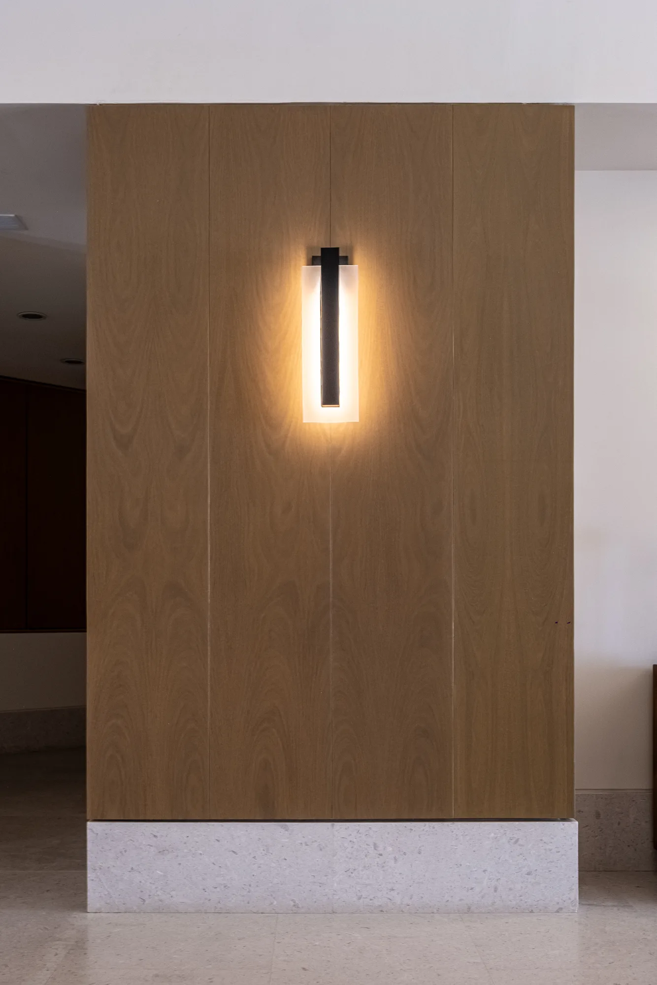 Detail of a wood-paneled feature wall with a backlit linear sconce over a terrazzo plinth