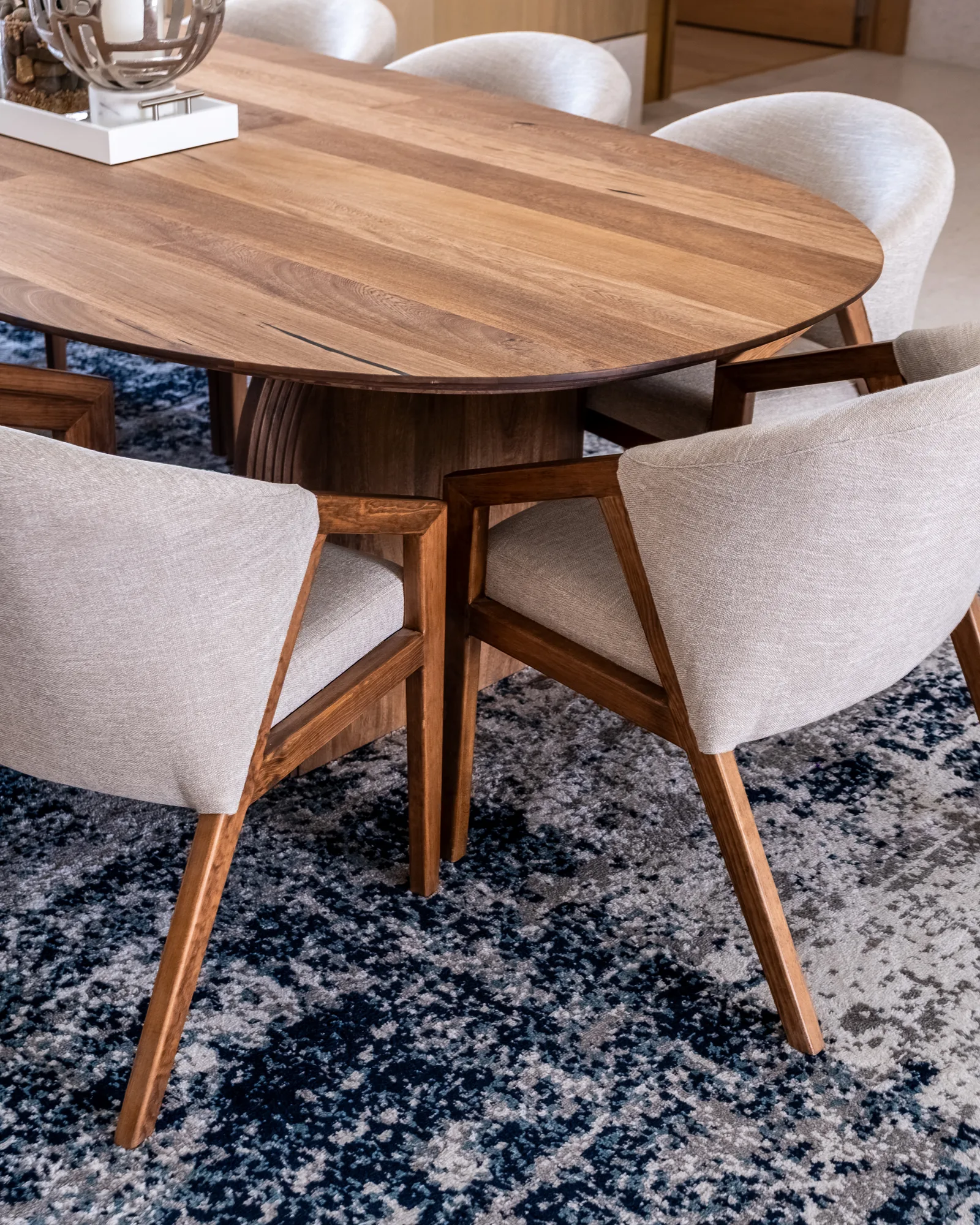 Close-up of the round walnut pedestal dining table and cream chairs on a blue rug