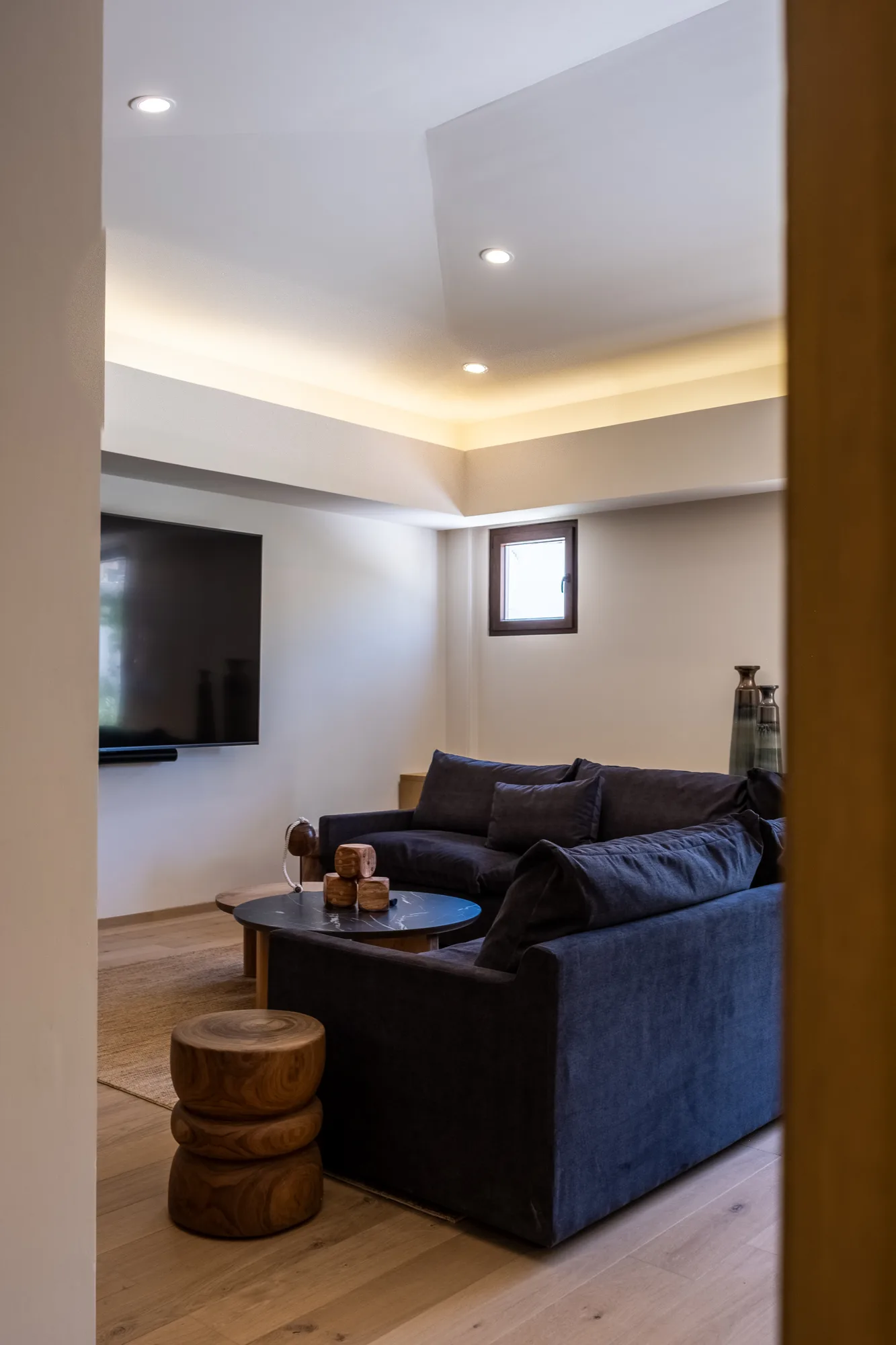 Media room with a navy velvet sectional, a round black marble table and carved wood stools under cove lighting