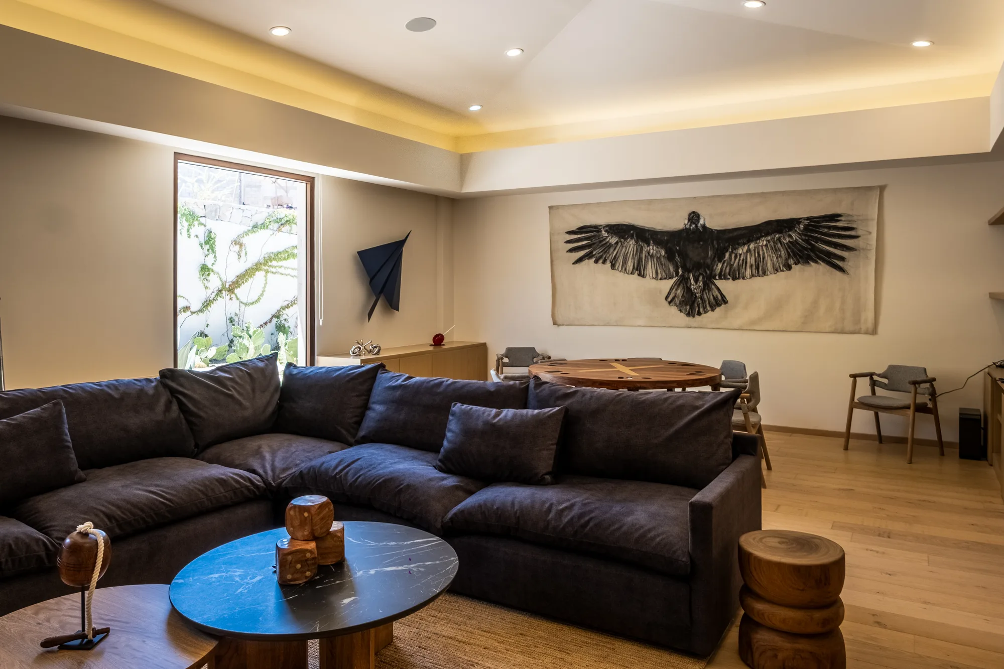 Family room with a suede sectional, a round marble table and a large condor artwork spanning the wall