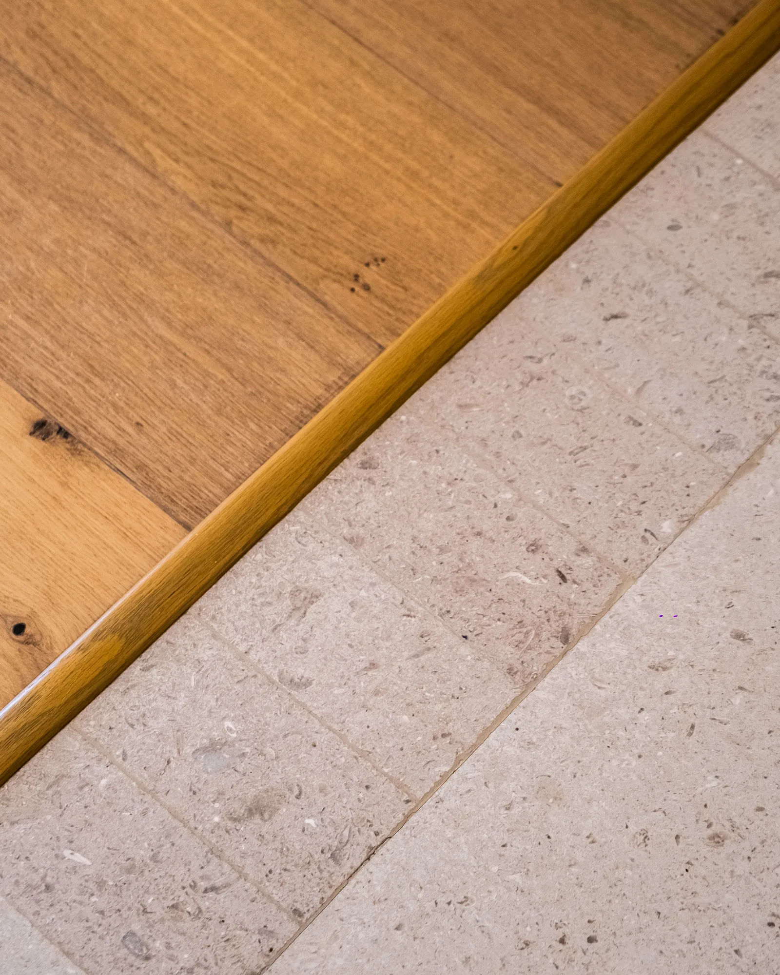 Detail of the floor transition where oak planks meet travertine tile along a brass threshold