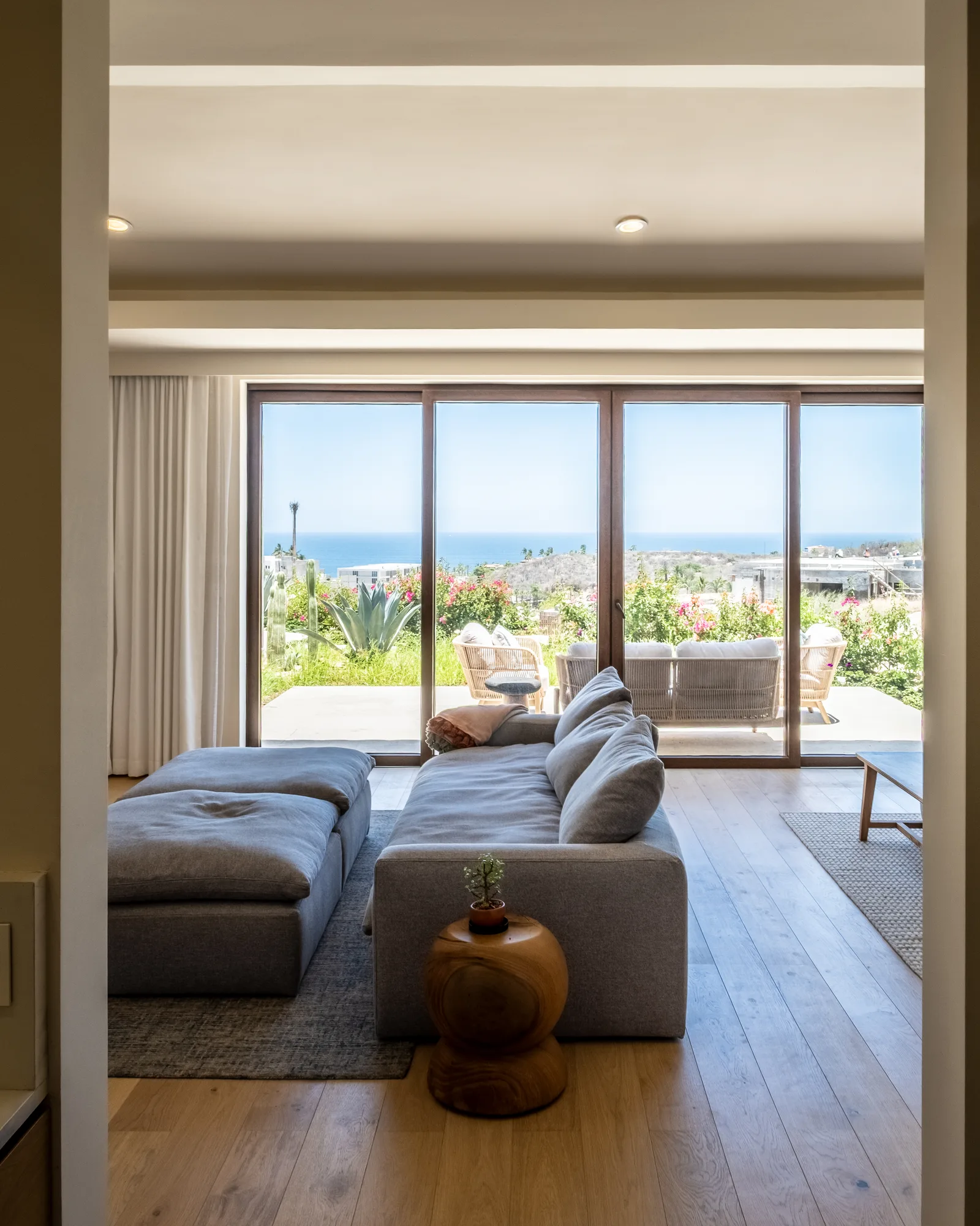 Living room with a grey sectional facing sliding glass doors that open to a terrace with agave and an ocean view