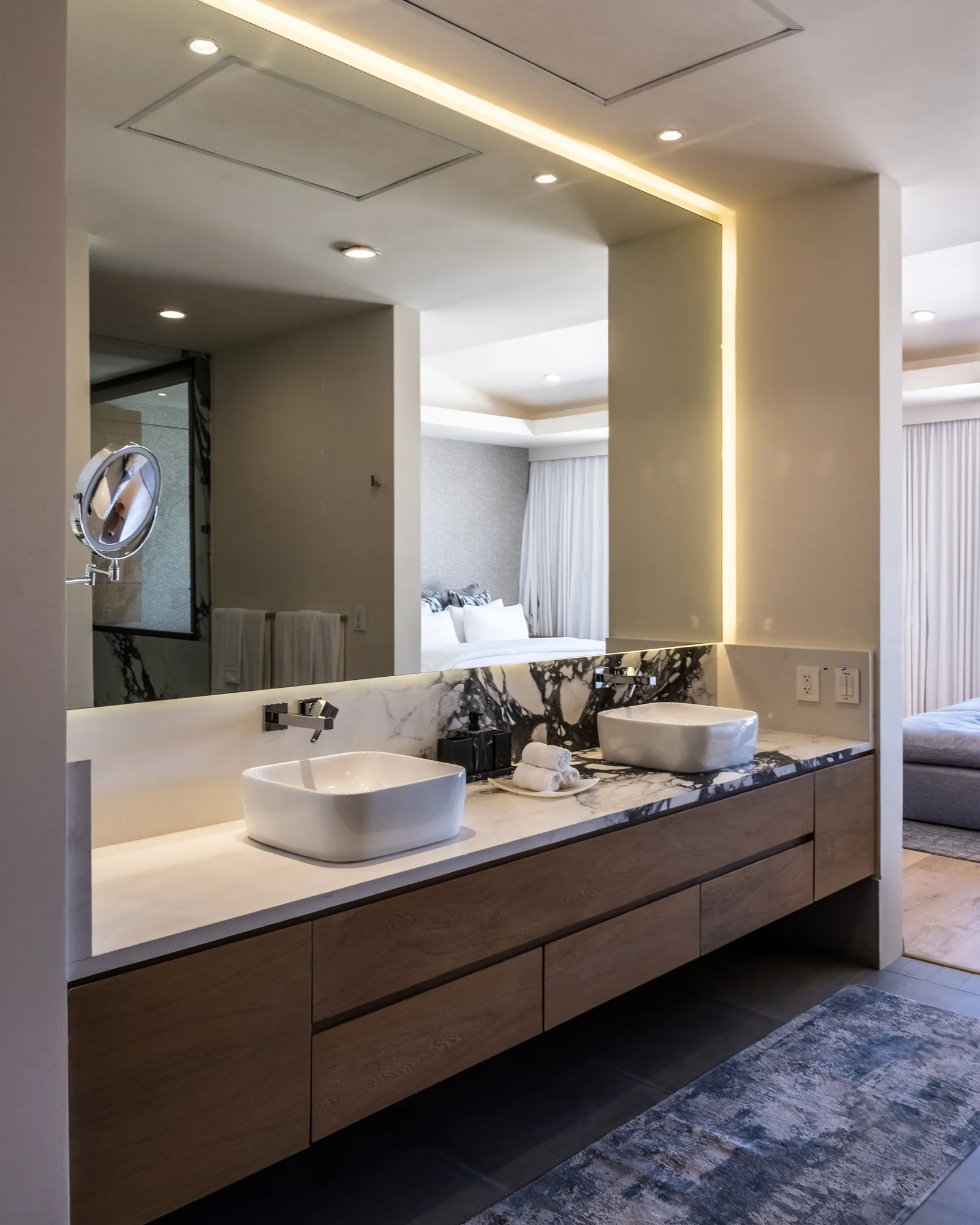 Primary bathroom with a floating wood double vanity, white vessel sinks and a black-and-white marble backsplash under a backlit mirror