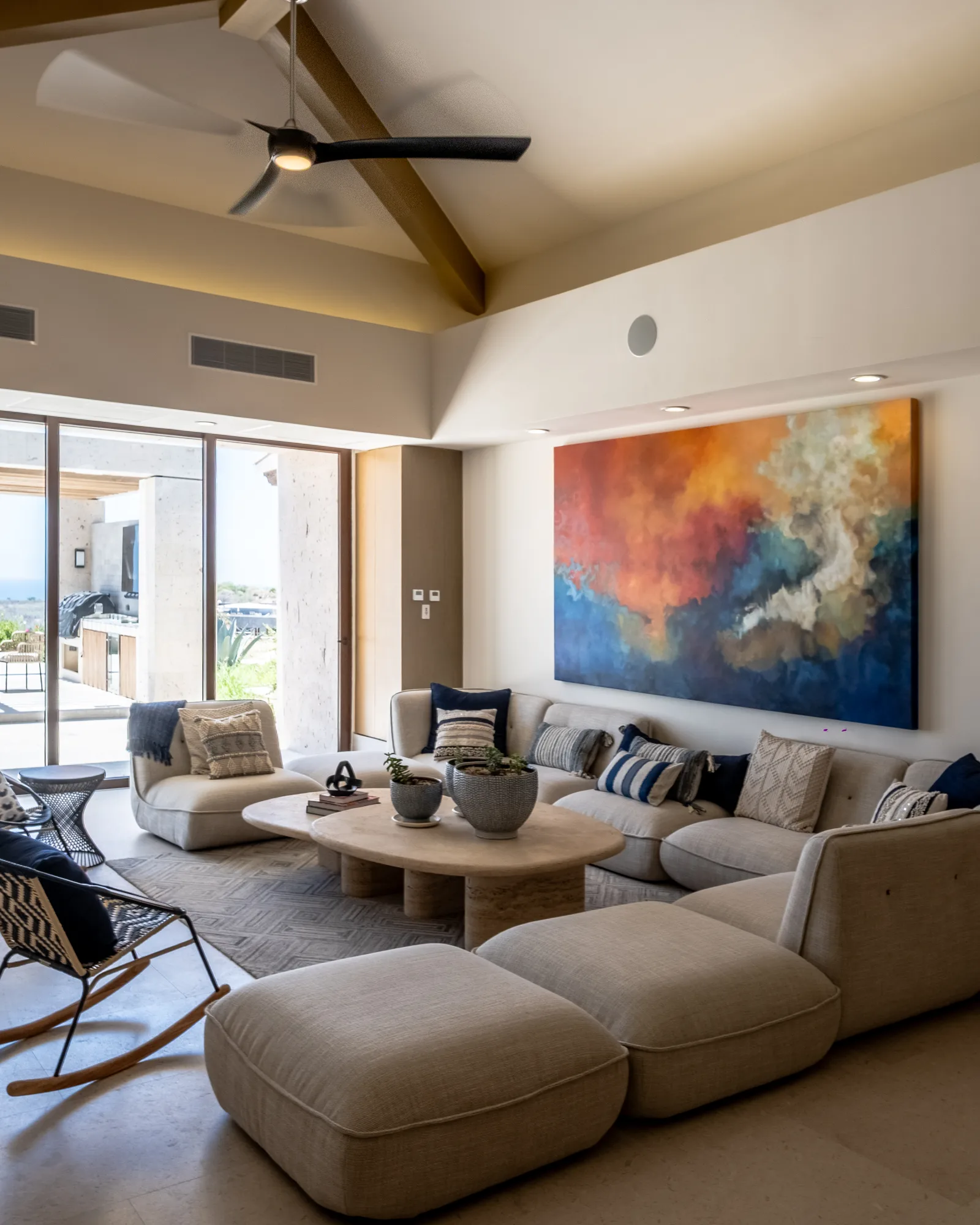 Great room under a beamed cathedral ceiling, with a beige modular sofa and a large orange-and-blue abstract painting, open to the sea