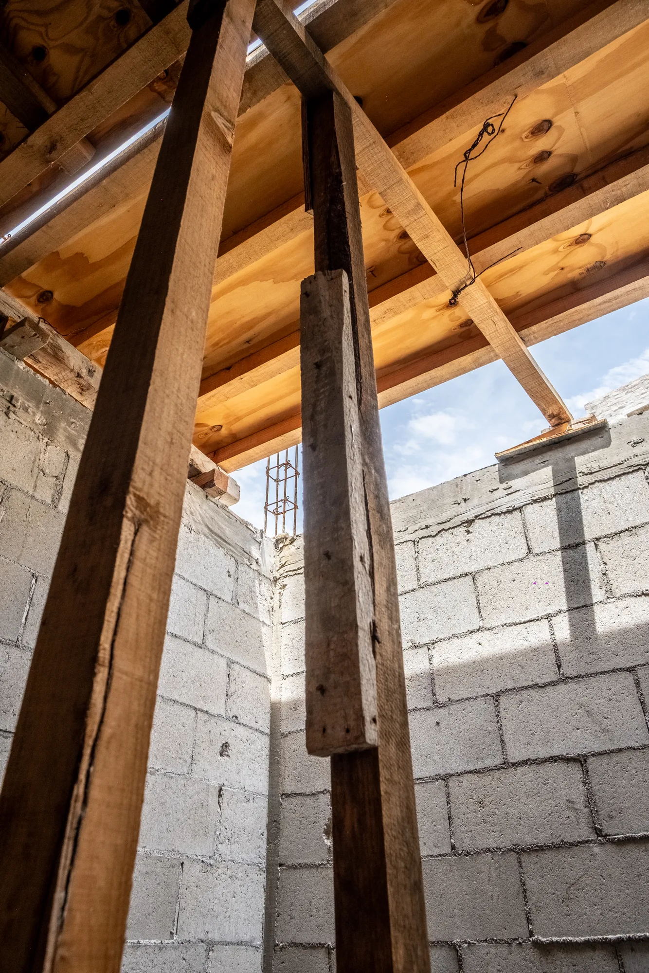 Looking up at timber props supporting a freshly formed slab beside a block wall and a patch of blue sky