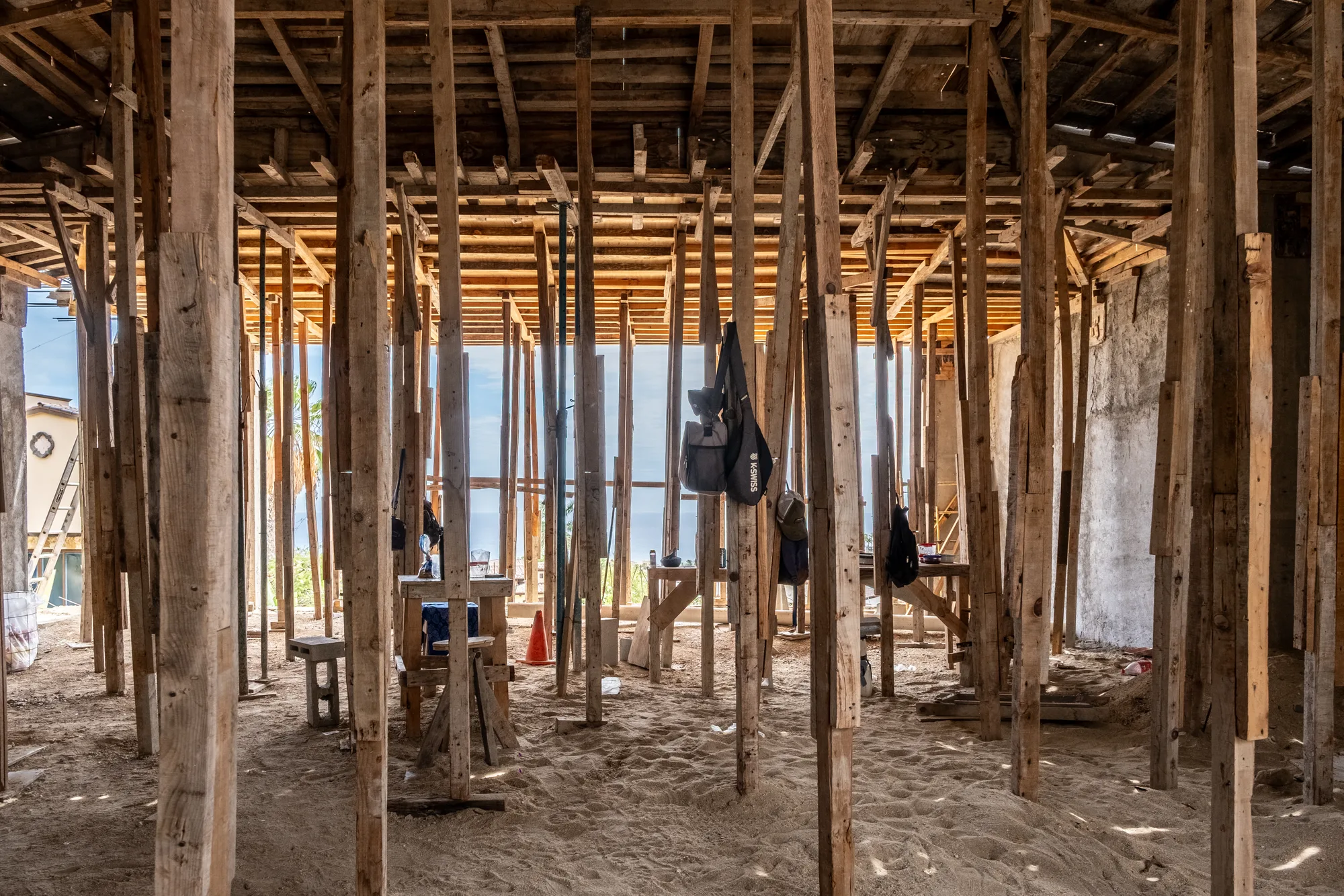 Wide interior view through a forest of timber shoring posts under the formwork ceiling, opening to the sea