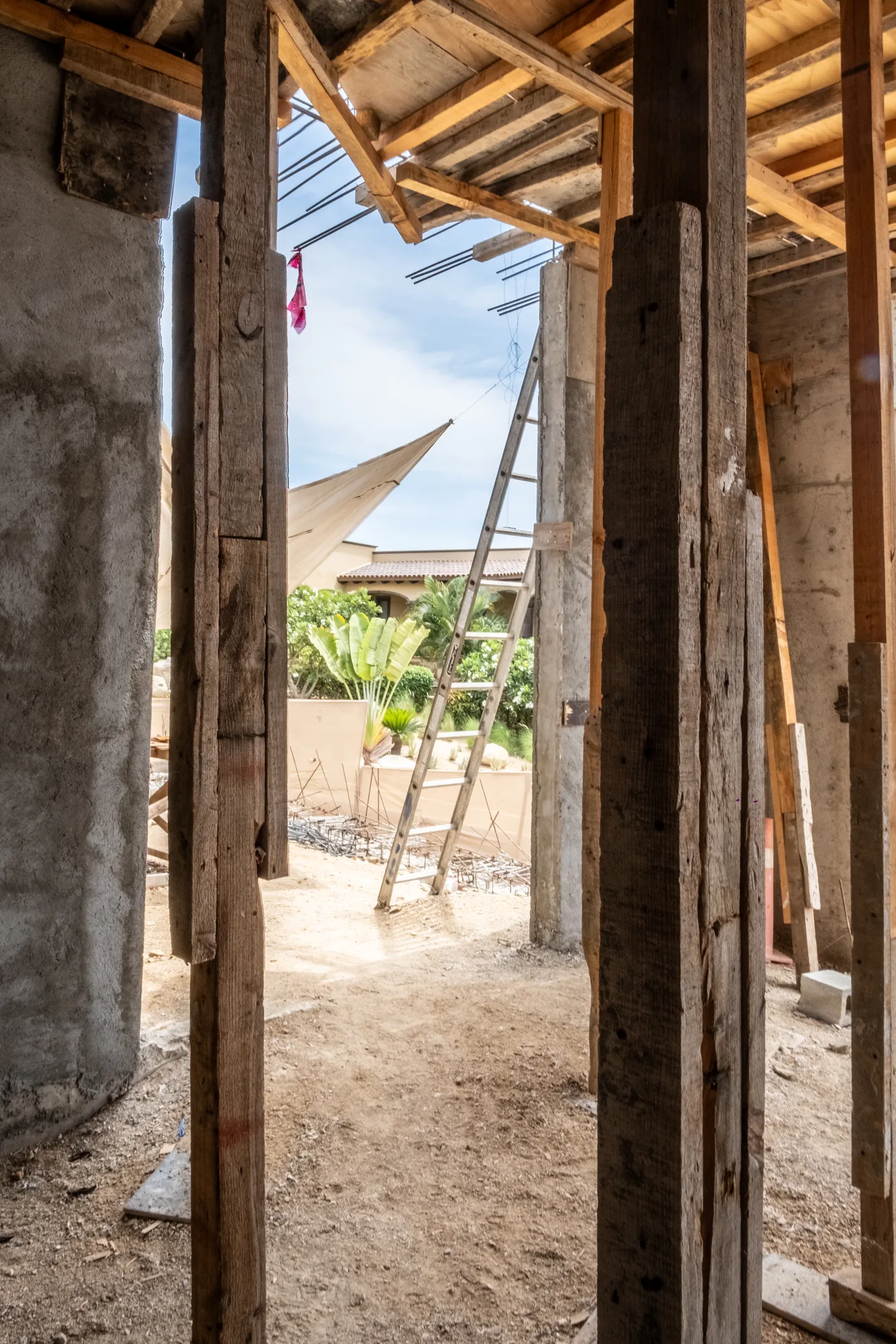 Timber-framed doorway opening onto the construction yard with a ladder, shade sail and garden
