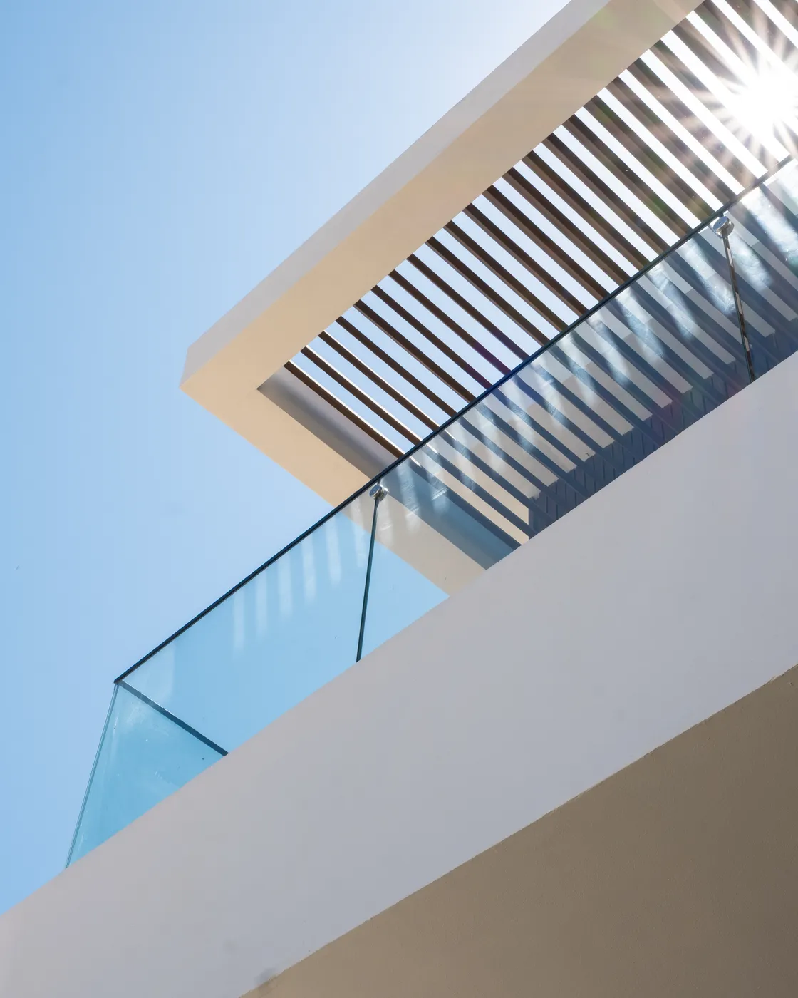 Looking up at a cantilevered roof with a wood-slat brise-soleil and glass balustrade against a bright sky