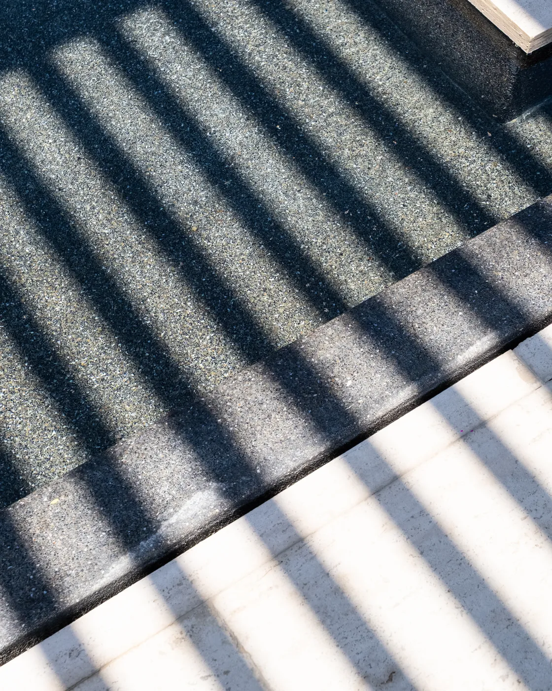 Abstract of louvered shadows striping a dark stone step and a white wall