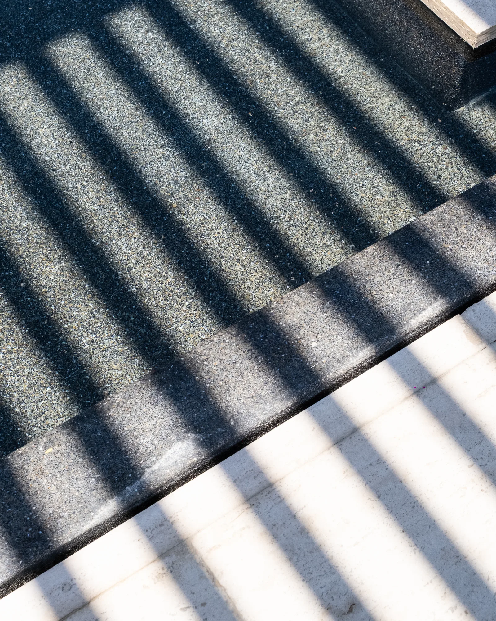 Abstract of louvered shadows striping a dark stone step and a white wall