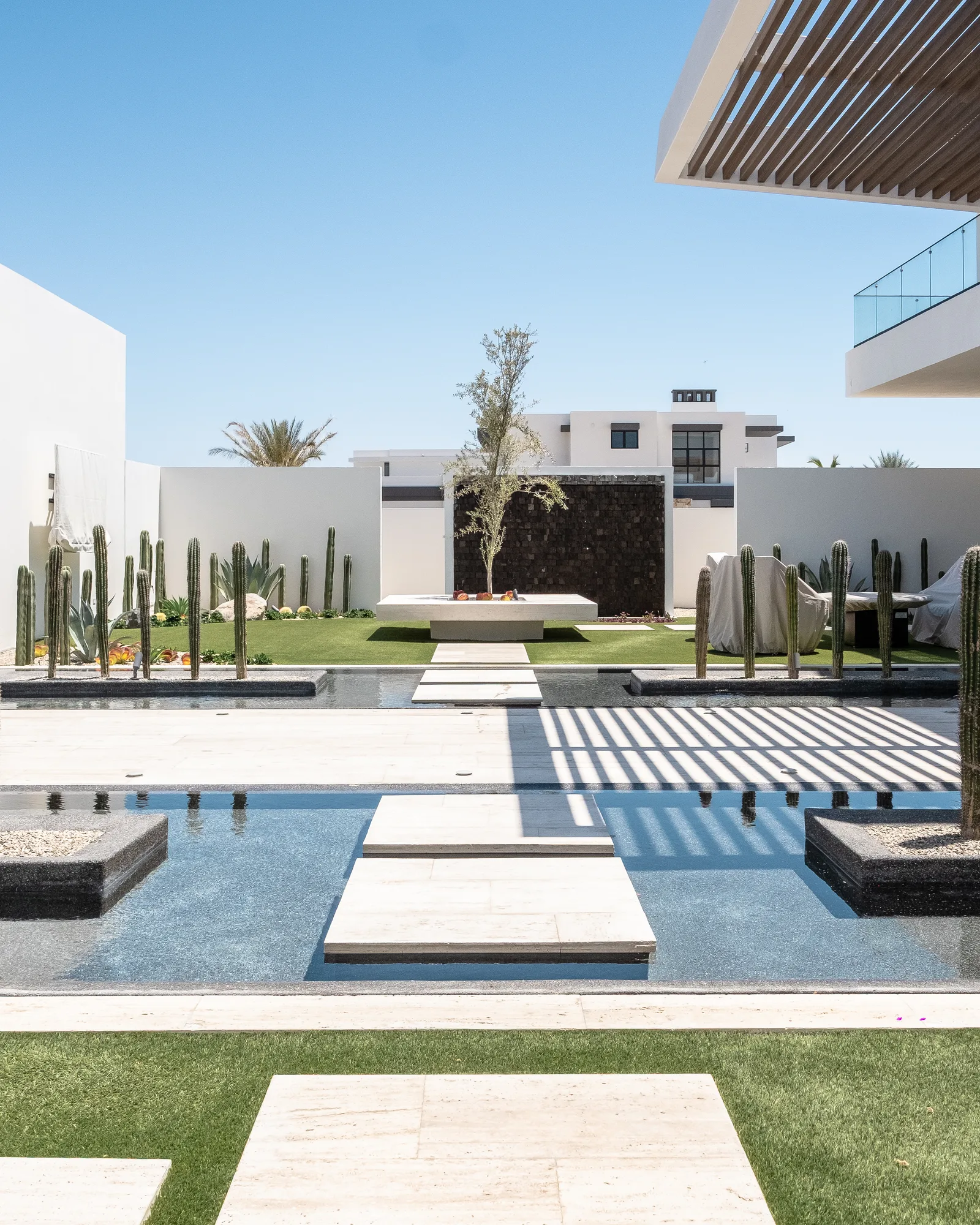 Courtyard of reflecting pools with travertine stepping stones, cactus gardens and a central fire feature under a slatted pergola