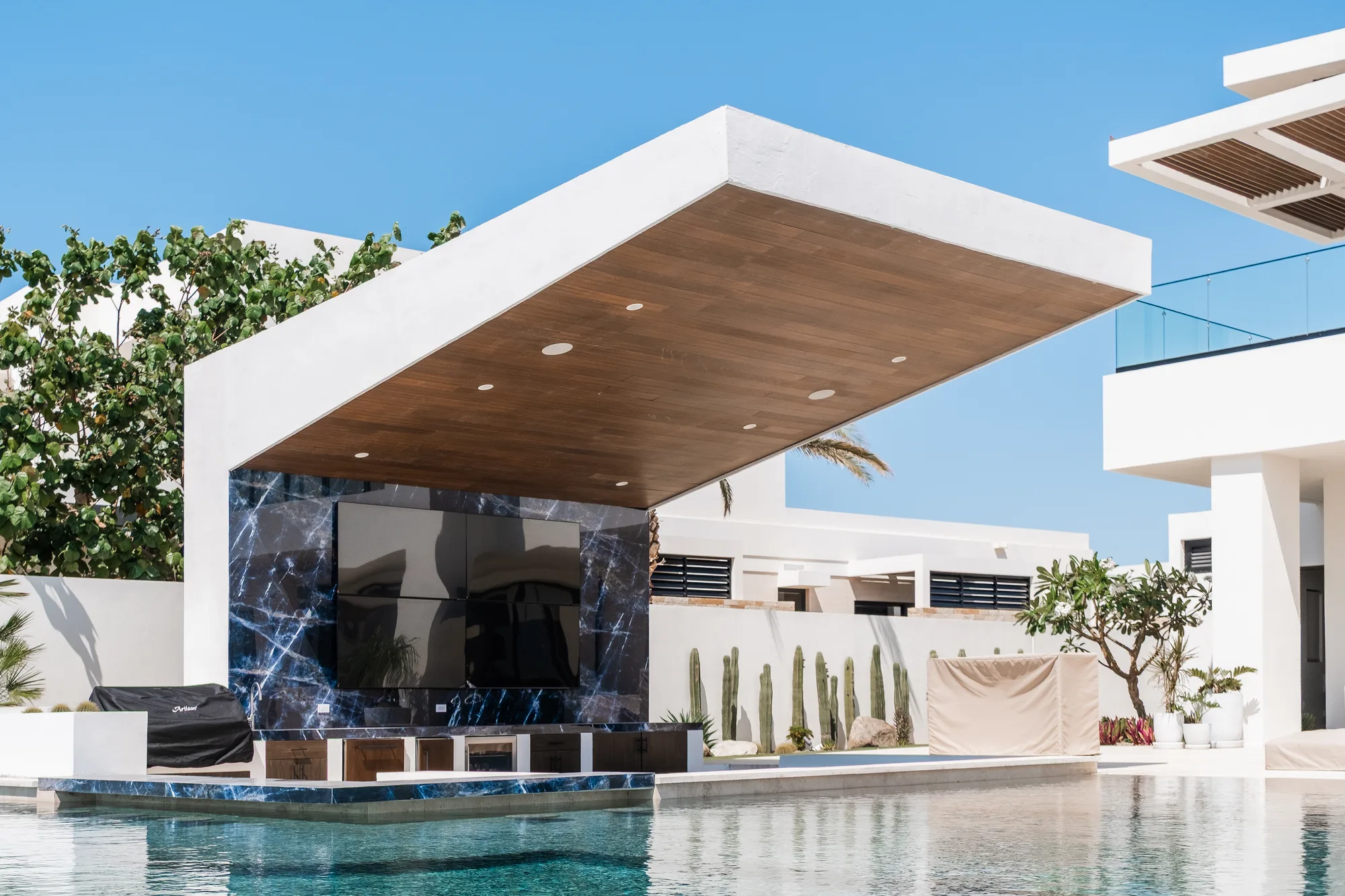 Poolside pavilion with a cantilevered wood-soffit roof and a black marble media wall beside the infinity pool