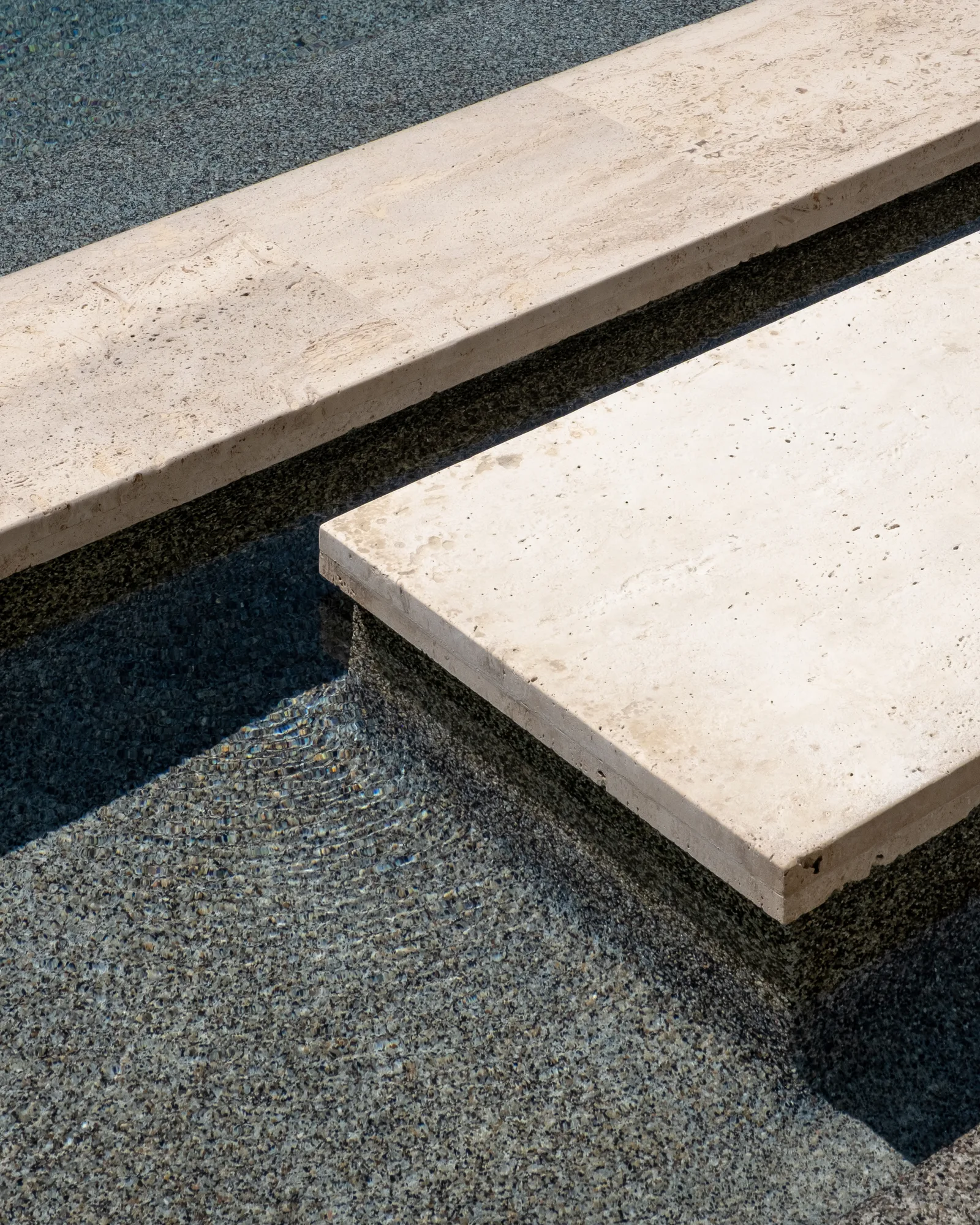 Abstract of travertine slab steps floating over a dark aggregate reflecting pool in strong light