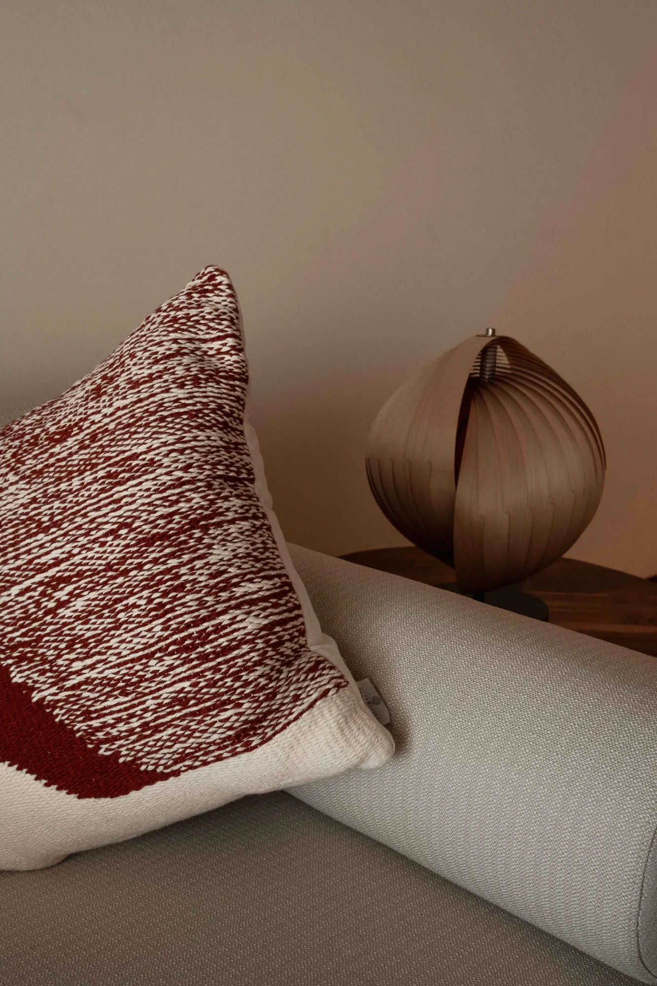 Detail of a rust-and-cream textured cushion beside a pleated wood orb table lamp