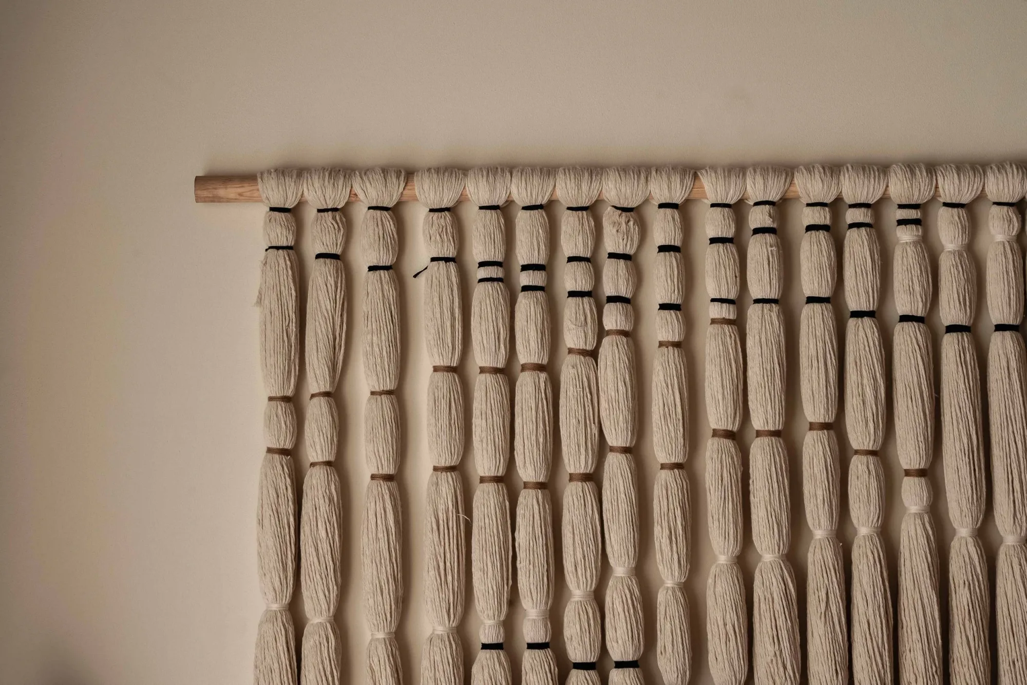 Detail of a cream macramé wall hanging with black accents on a wooden dowel