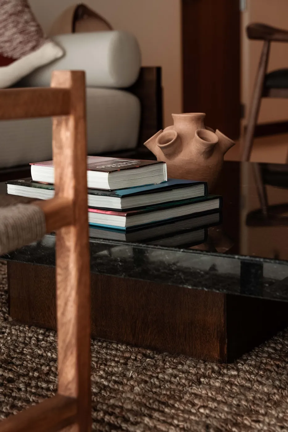 Styling detail of stacked books and a twin-spout clay vessel on a black marble table over a jute rug