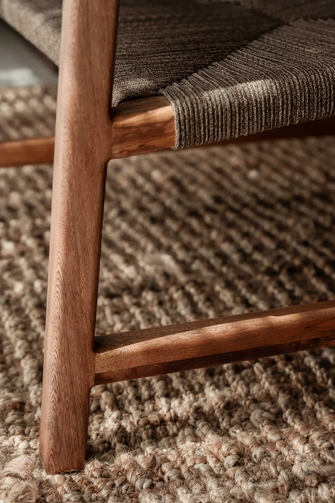 Close-up of a teak chair leg and woven-cord seat resting on a jute rug