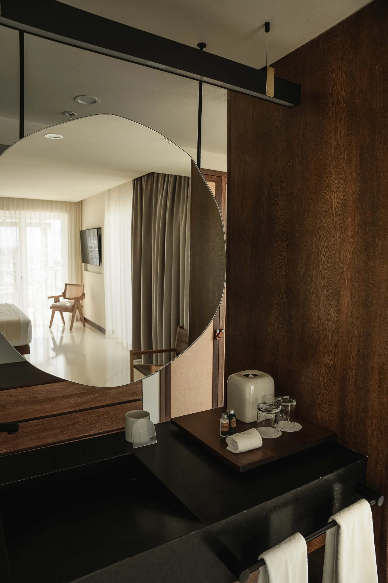 Guest room reflected in a round mirror above a black vanity with amenities, a leather-clad wall alongside