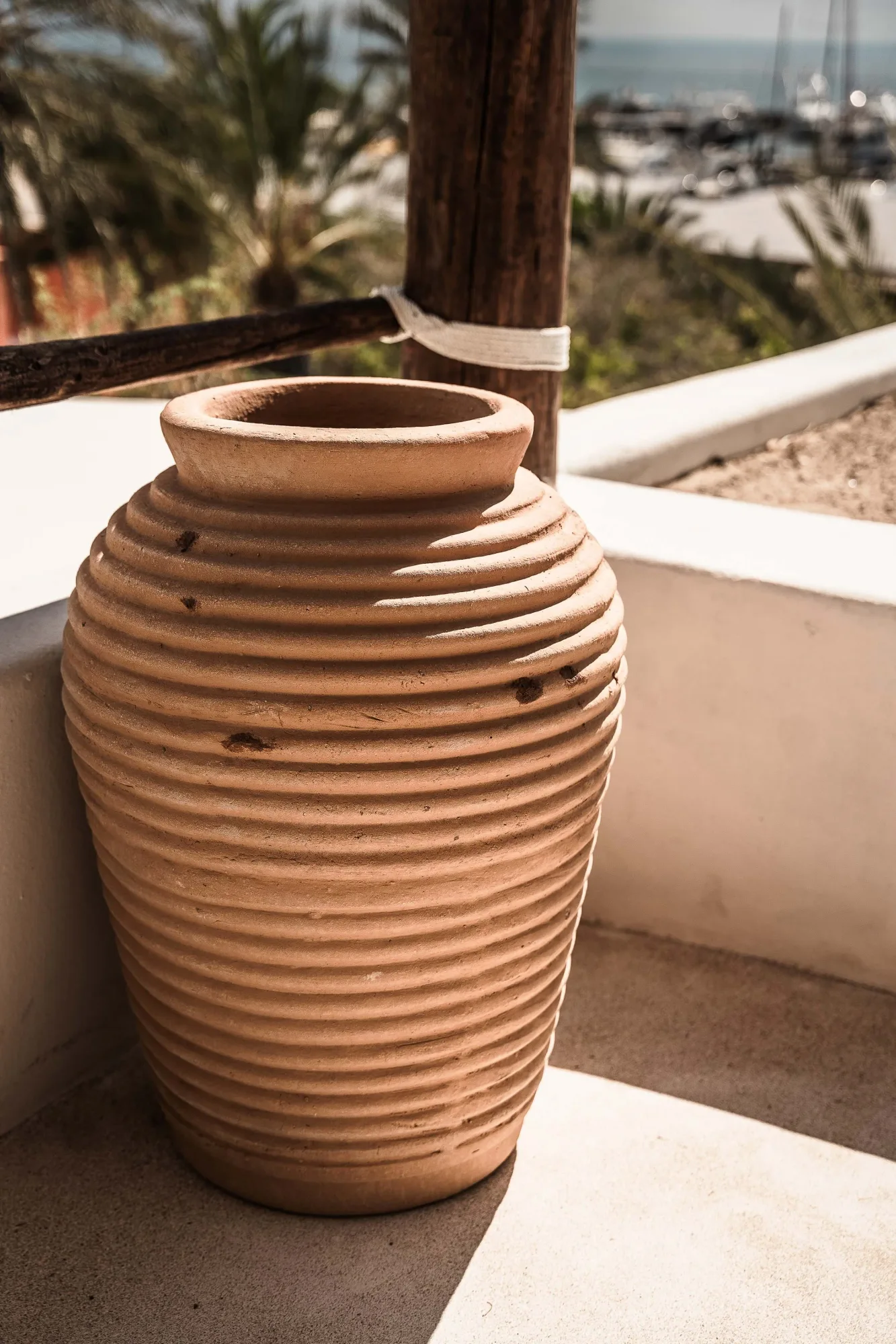 Ribbed terracotta jar on a plaster terrace by a timber post, overlooking palms and the marina on the Bay of La Paz
