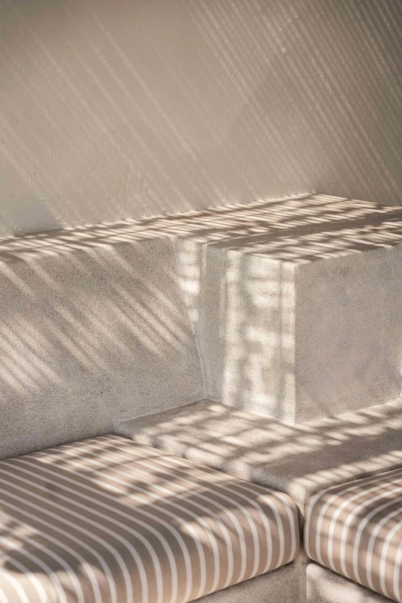 Striped light from a reed roof falling across plaster benches with striped cushions