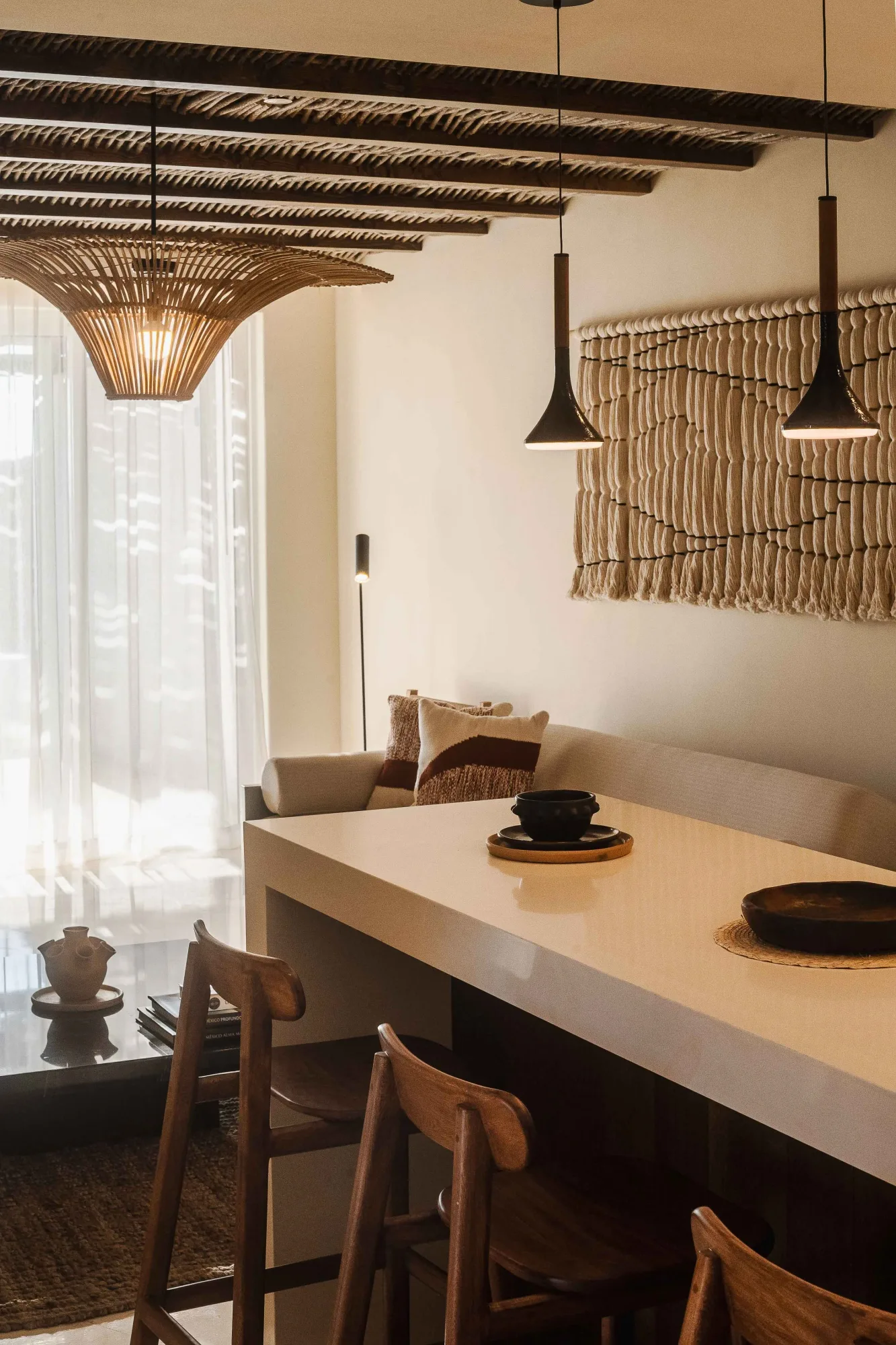 Suite kitchenette with a rattan pendant and dark cone lights over a stone counter with wood stools and macramé art