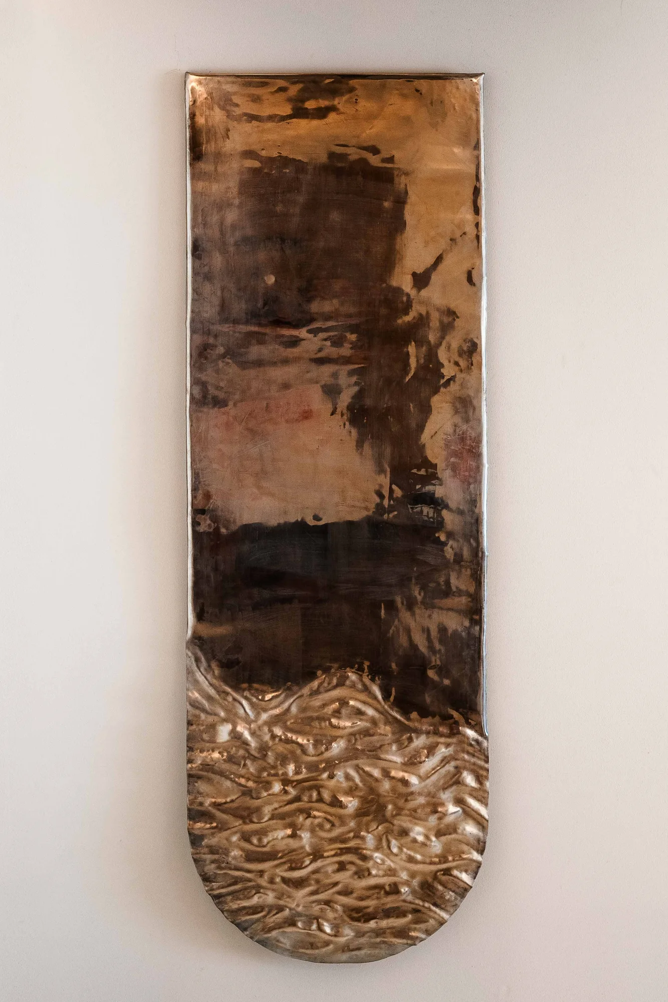 Detail of a textured bronze wall panel with a rippled molten lower half on a plaster wall
