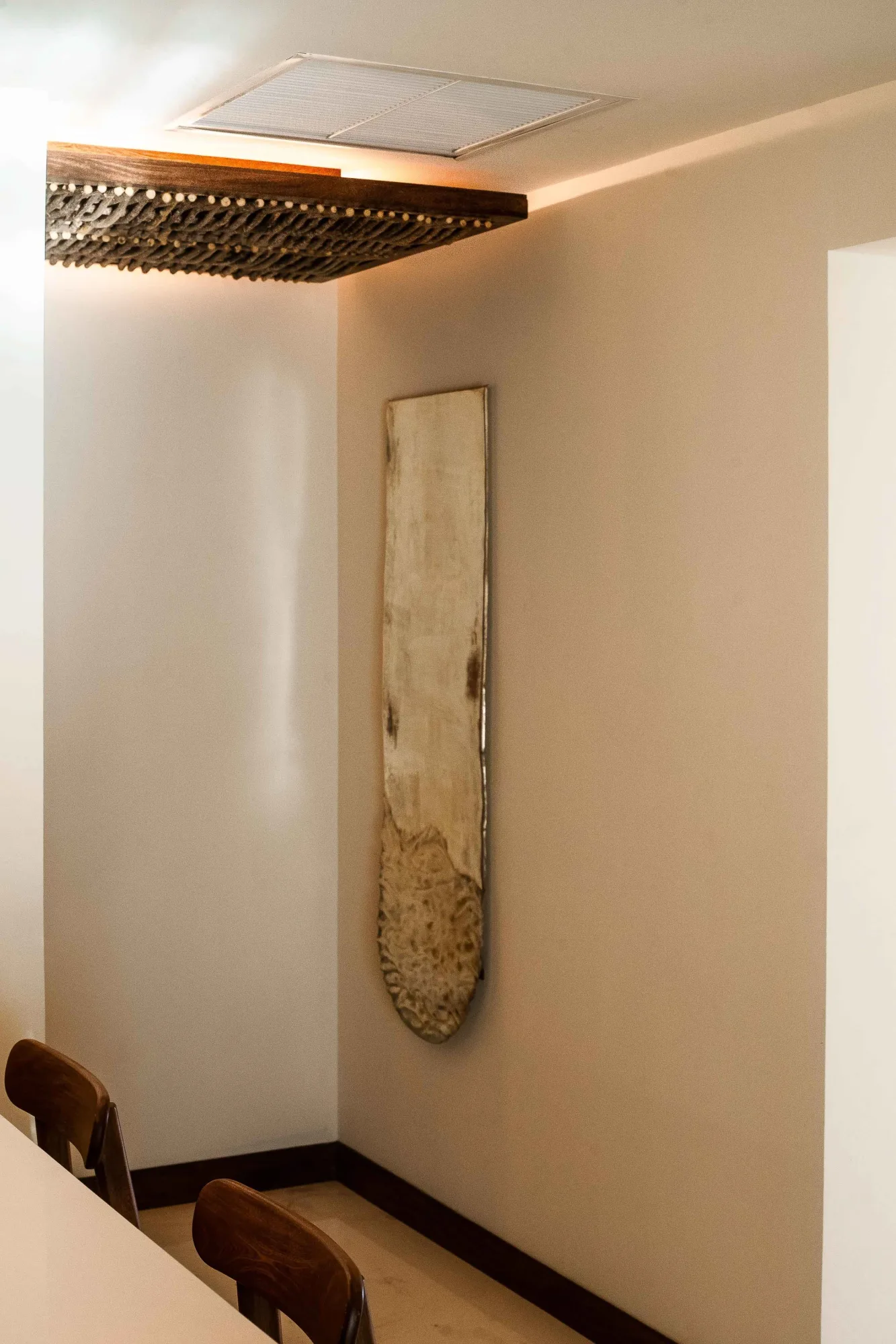 Corner with a rustic wood wall panel beside a backlit reed ceiling box and wood chairs