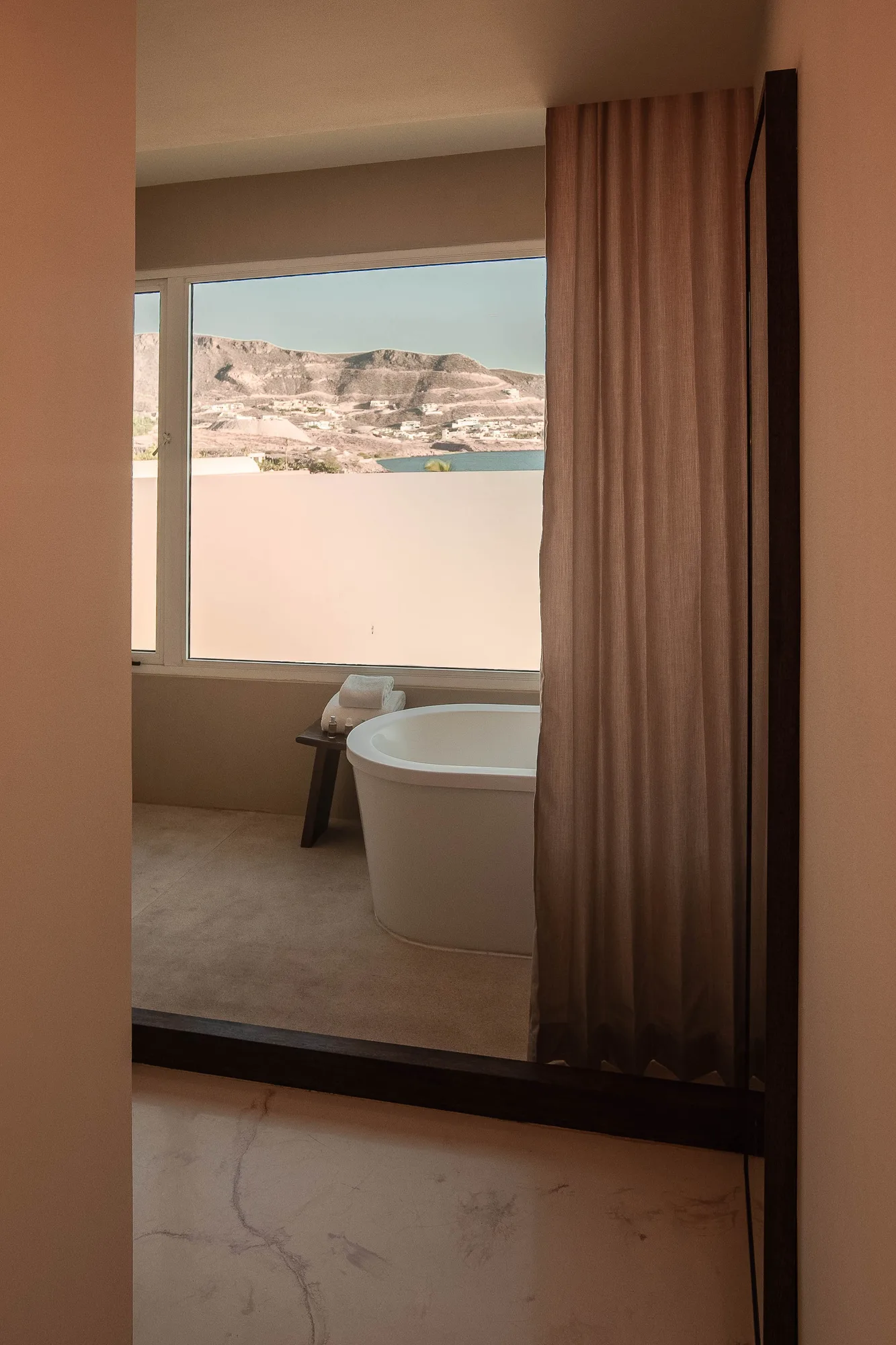 Freestanding tub glimpsed through a doorway at a window with a bay and mountain view