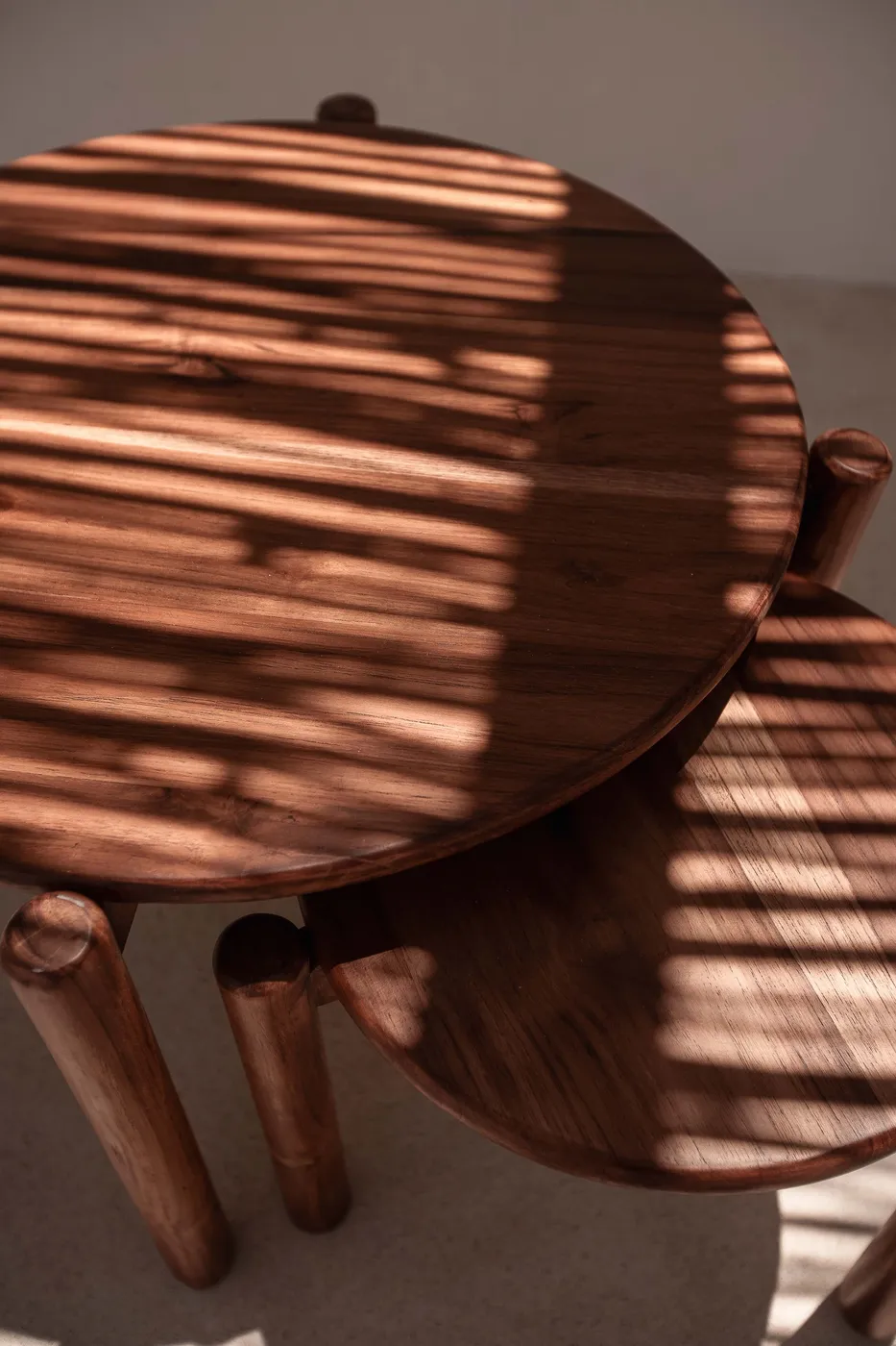 Overhead detail of round walnut tables with striped light raking across the grain