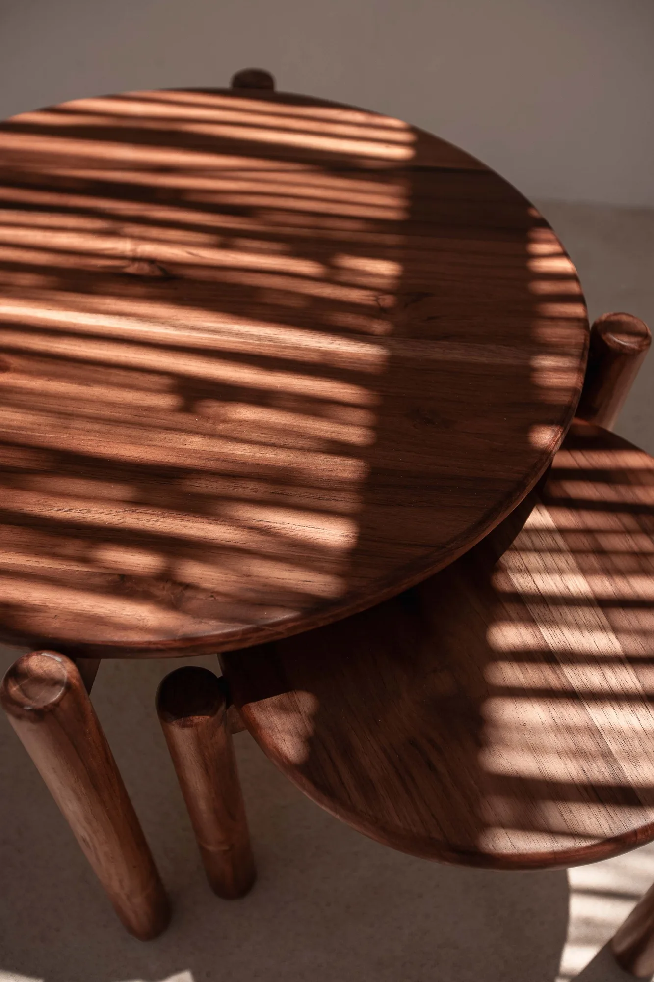 Overhead detail of round walnut tables with striped light raking across the grain