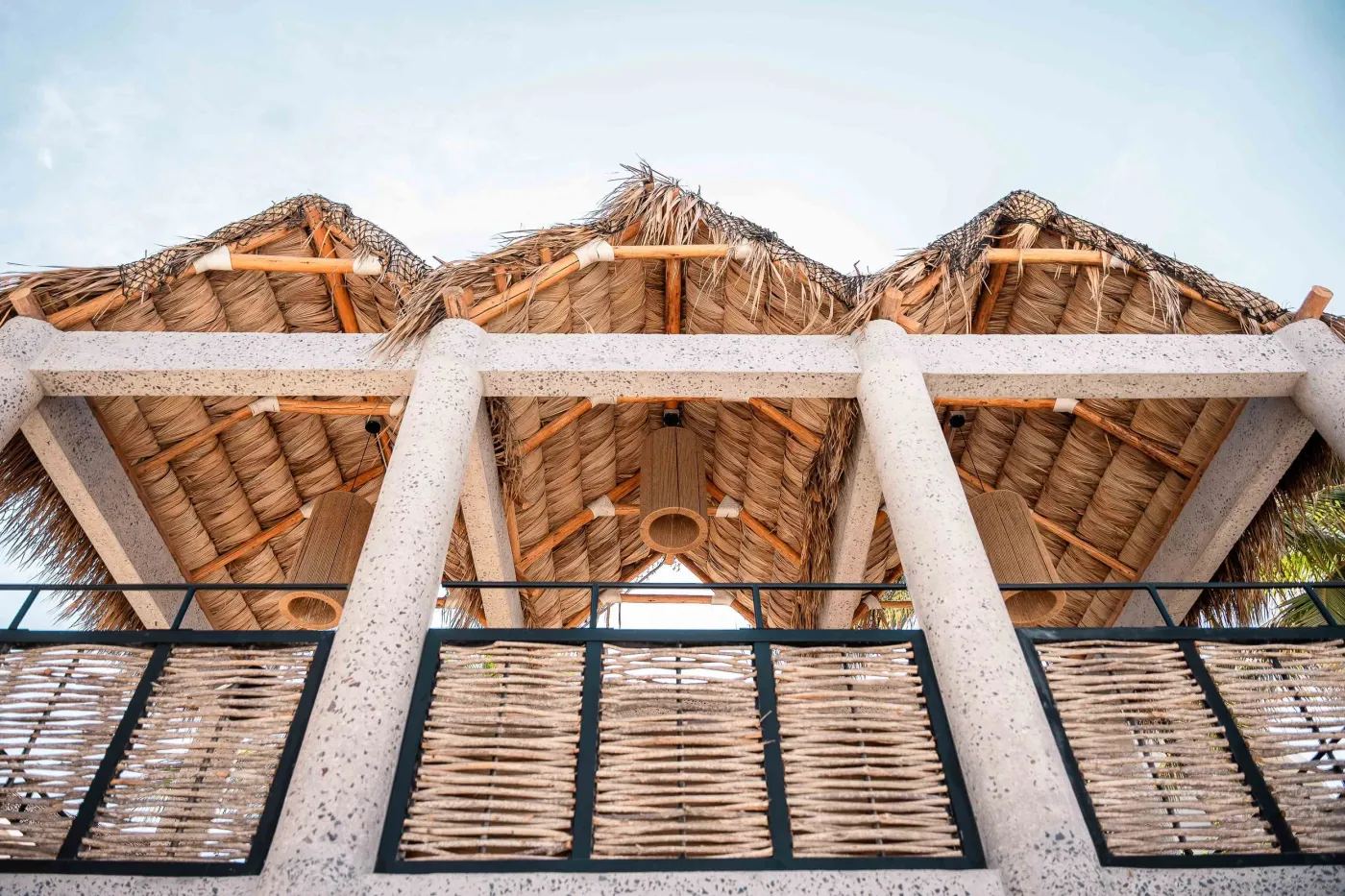 Looking up at the palm-thatch palapa roof on terrazzo columns and timber beams with woven railings, Puerto Beach Club in La Paz