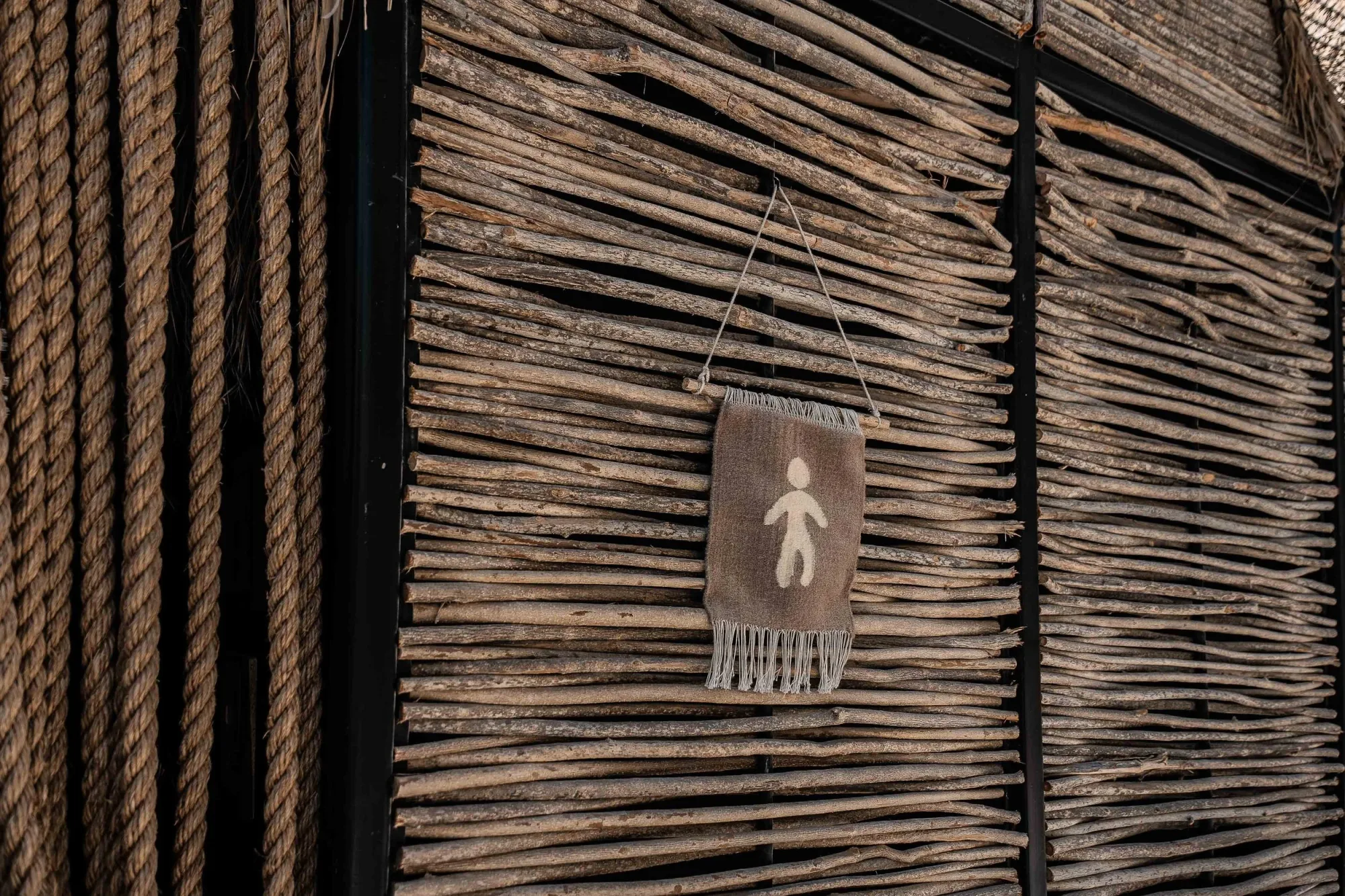 Detail of a burlap restroom sign with a printed figure hanging on a black-stained stick wall