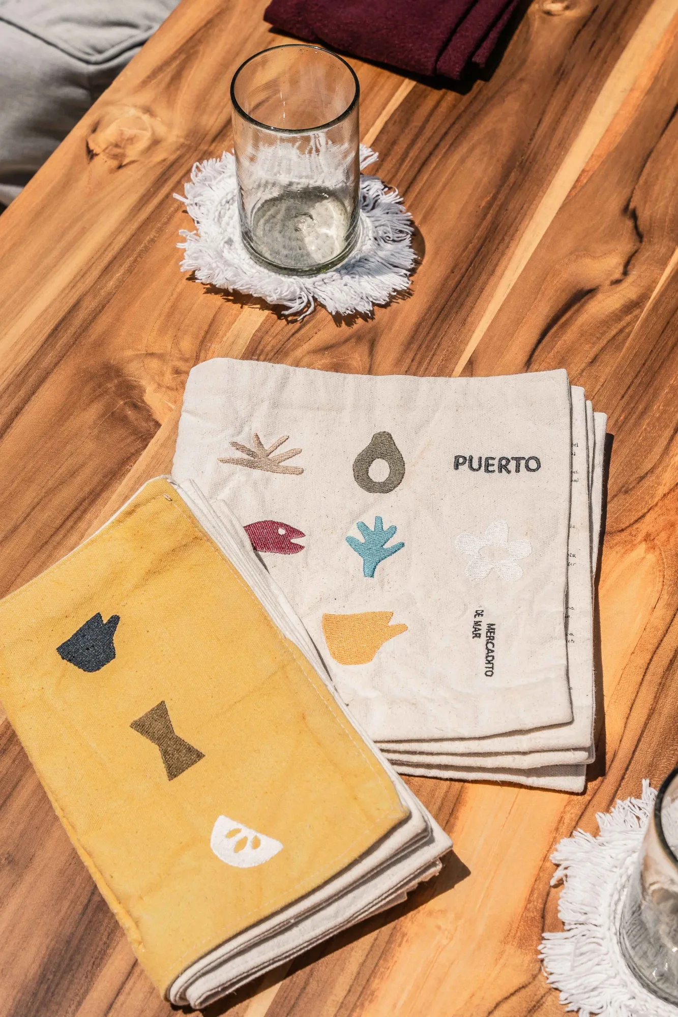 Branding detail of cotton napkins printed with Puerto and small Baja icons on a teak table
