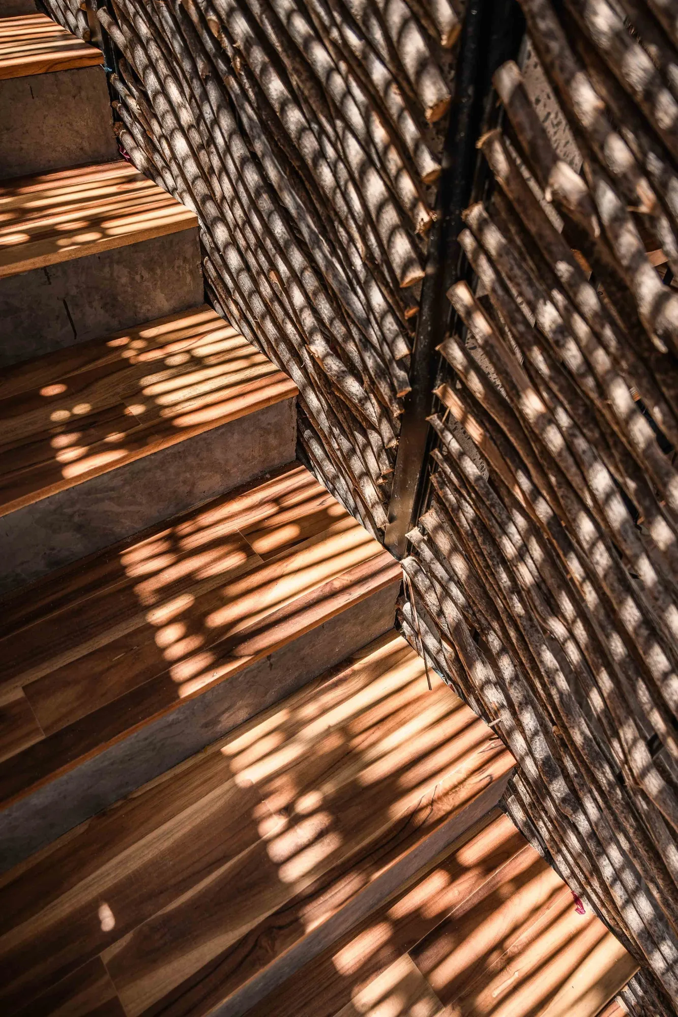 Abstract of dappled light through thatch falling on a wood staircase beside an ocotillo-stick wall