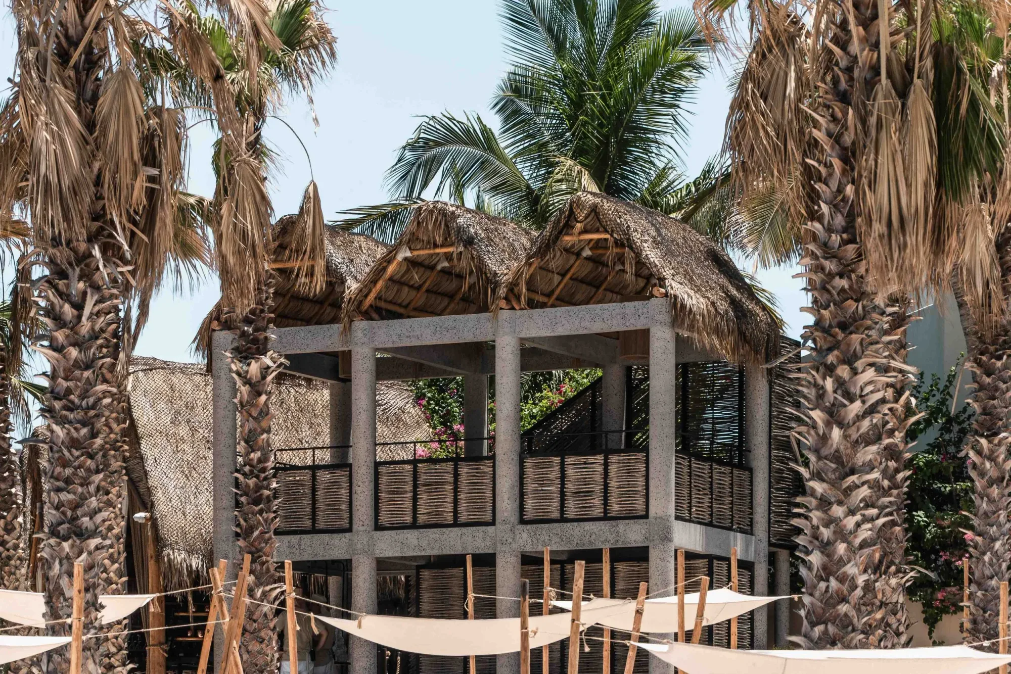 The two-story palapa tower of the beach club framed by palms above canvas shade sails