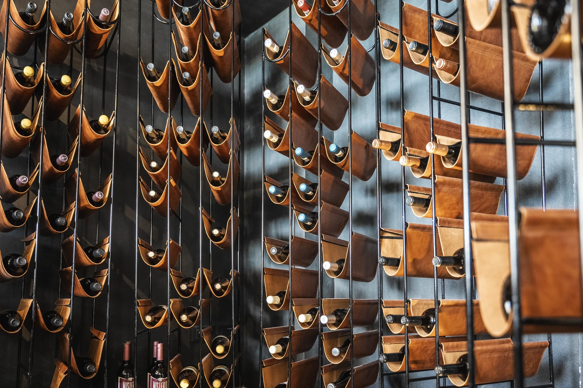 Wine wall of leather cradles on black metal rails holding bottles, Quemadero on the La Paz malecón