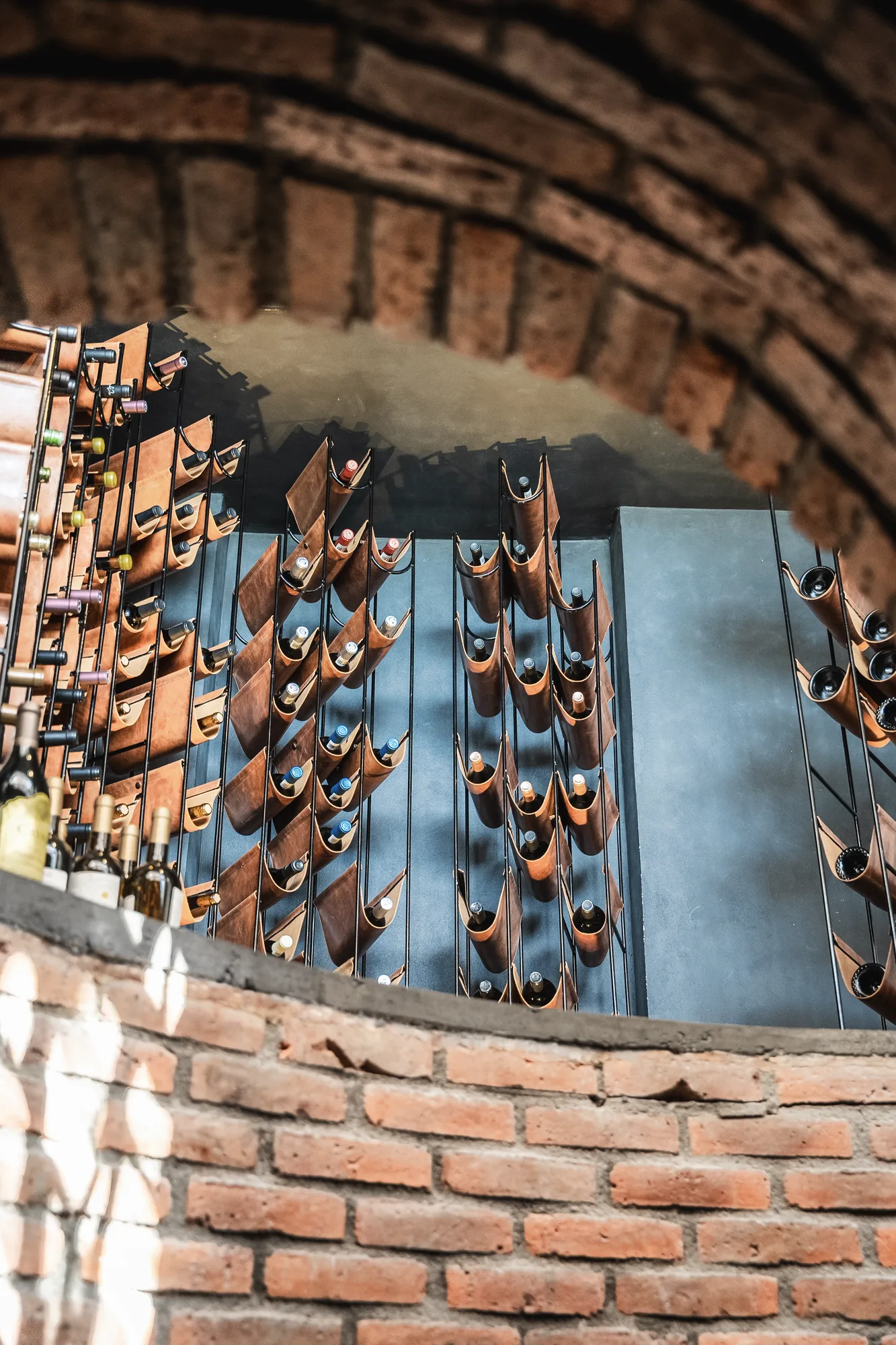 Wine cellar under a brick barrel vault, bottles resting in leather cradles on a blue-grey wall