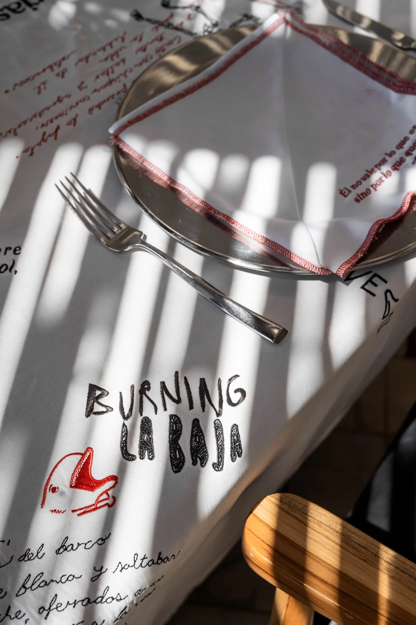 Close-up of the signature Burning La Baja linen with a red drawing and script, a fork and folded napkin in striped light