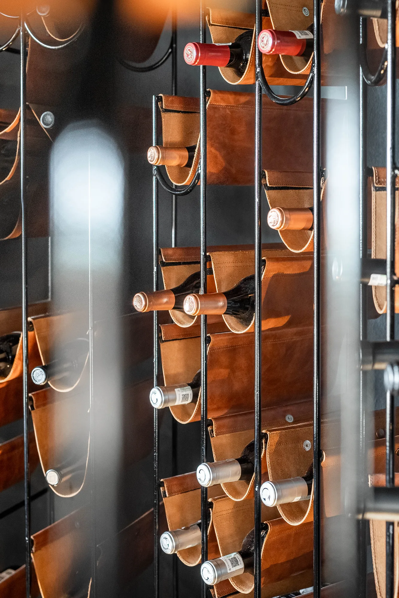 Close-up of the wine wall, bottles held in leather cradles on black rails with a red bottle standing out